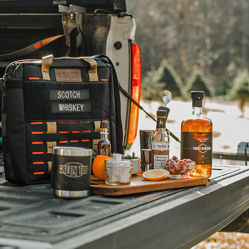 Bourbon Bag (made in the USA by Blue Ridge Overland Gear) on tailgate of truck with outdoor scene in the background.