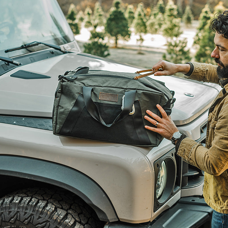 Man with TOUR Duffel (made in the USA by Blue Ridge Overland Gear) next  to off-road vehicle on a Christmas tree farm.