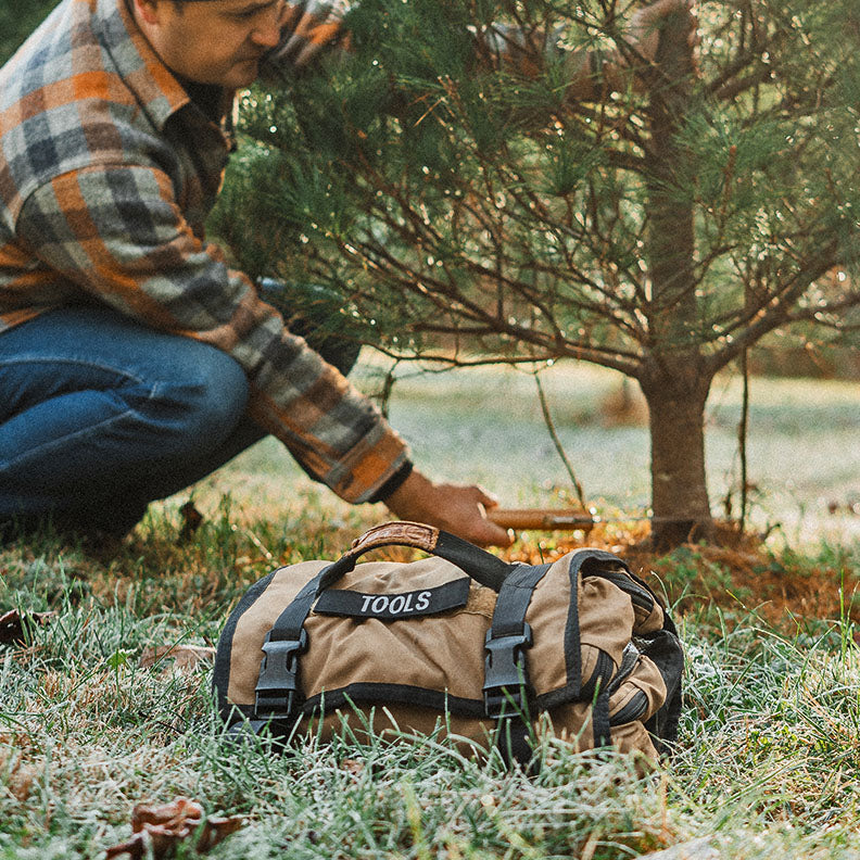 Man cuts down a Christmas tree with the Tool Roll (made in the USA by Blue Ridge Overland Gear) in the foreground.